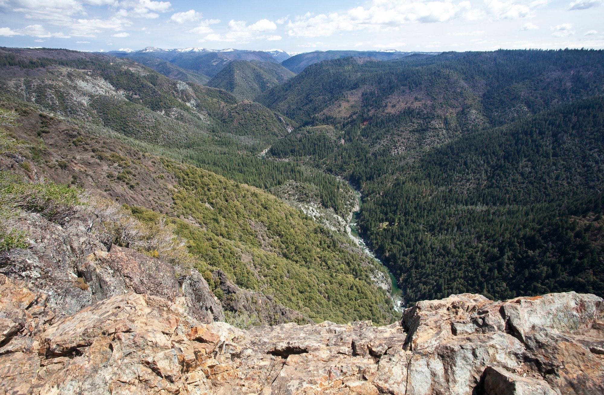 The North Fork American River carving through its forested gorge, seen from the canyon rim with the snow-capped Sierra crest beyond